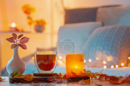 Téléchargez les photos : Thermo verre avec thé chaud dans la chambre de nuit sombre avec des feuilles automnales - en image libre de droit