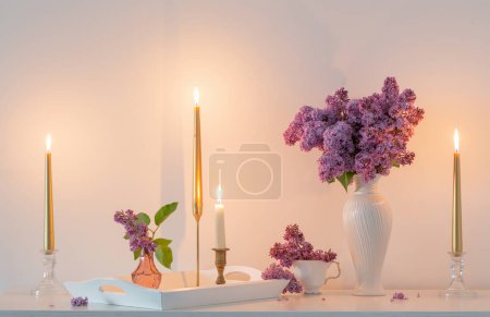 Téléchargez les photos : Fleurs lilas en vase blanc et bougies dorées sur fond blanc mur - en image libre de droit