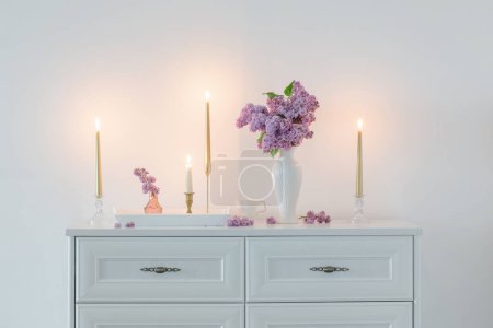 Foto de Flores lila en jarrón blanco y velas doradas sobre fondo pared blanca - Imagen libre de derechos