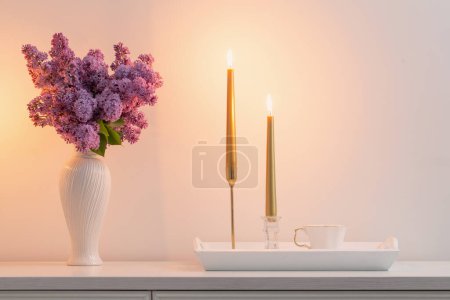 Photo for Lilac flowers in white vase and golden candles on background white wall - Royalty Free Image