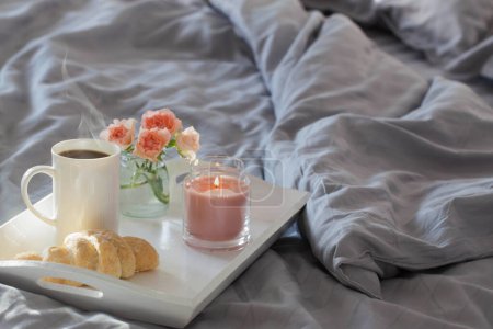 Téléchargez les photos : Tasse de café avec croissant et roses roses sur le lit dans la chambre - en image libre de droit