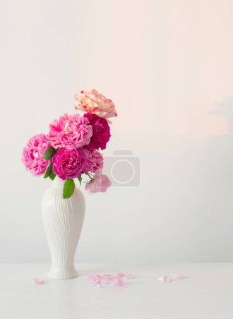 Pink roses in white vase on table  on background white wall