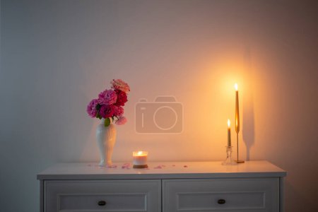 Téléchargez les photos : Roses roses dans un vase et une bougie allumée sur fond blanc mur - en image libre de droit