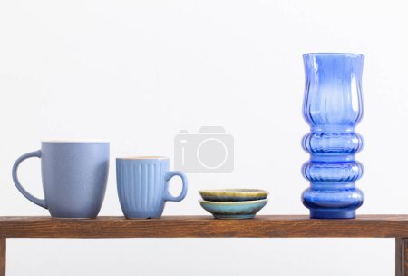 Téléchargez les photos : Tasses bleues et vase en verre sur étagère en bois sur fond blanc - en image libre de droit
