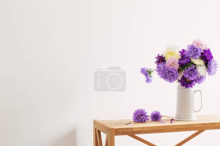 Téléchargez les photos : Beau bouquet d'asters en cruche blanche sur fond mur blanc - en image libre de droit