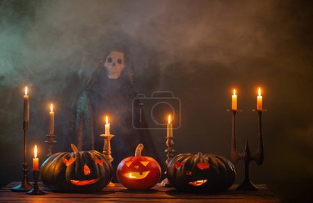 Foto de Calabazas de halloween con velas encendidas y la muerte en el manto sobre fondo oscuro - Imagen libre de derechos