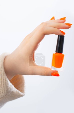 Foto de Manos femeninas con manicura naranja con botella de esmalte de uñas sobre fondo blanco - Imagen libre de derechos