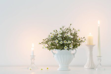 Foto de Flores blancas en jarrón de cerámica blanca con velas encendidas en el interior blanco - Imagen libre de derechos