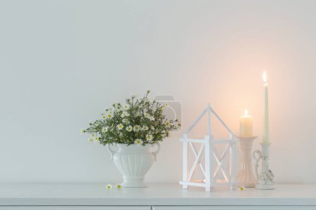 Photo for White flowers in white ceramic vase with burning candles in white interior - Royalty Free Image