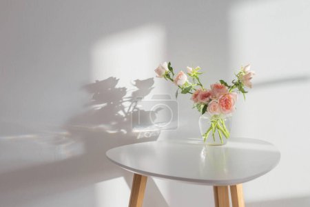 Foto de Rosas rosadas en tarro de cristal sobre mesa blanca moderna sobre fondo pared blanca - Imagen libre de derechos
