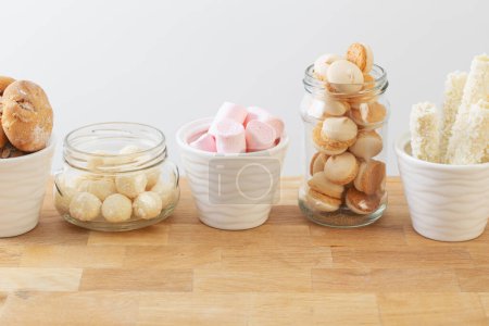 Téléchargez les photos : Bonbons et biscuits dans des pots sur une étagère en bois sur fond blanc - en image libre de droit