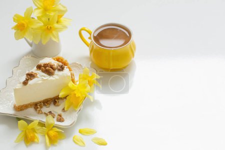 Foto de Tarta de queso con taza de té y flores amarillas de primavera sobre una mesa blanca - Imagen libre de derechos