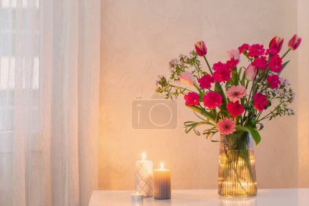 Téléchargez les photos : Fleurs roses en verre vase moderne avec des bougies brûlantes à l'intérieur blanc - en image libre de droit