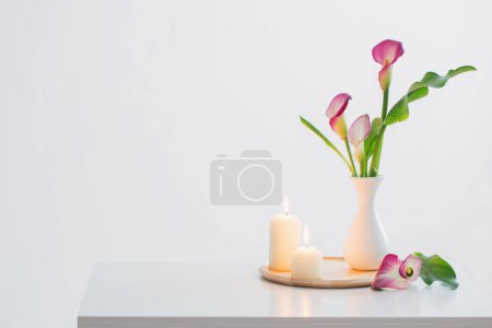 Téléchargez les photos : Lys de calla rose dans un vase et bougies allumées sur fond blanc - en image libre de droit