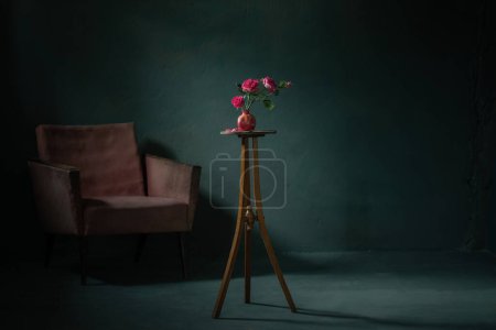 Foto de Rosas rosadas en jarrón rosa con sillón viejo en la pared oscura de fondo - Imagen libre de derechos