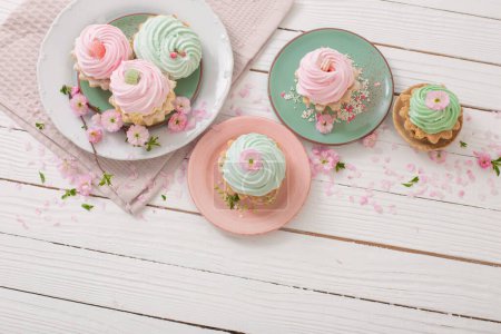 Foto de Cupcakes rosas y verdes con flores de primavera sobre fondo blanco de madera - Imagen libre de derechos