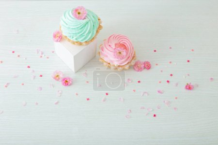 Téléchargez les photos : Cupcakes roses et verts avec des fleurs printanières sur des podiums en bois sur fond blanc - en image libre de droit