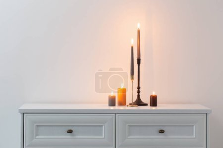 Photo for Burning candles on white wooden shelf in white interior - Royalty Free Image