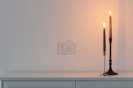 Photo for Burning candles on white wooden shelf in white interior - Royalty Free Image