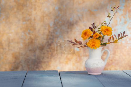 Foto de Flores de crisantemo en jarra sobre fondo pared vieja a la luz del sol - Imagen libre de derechos
