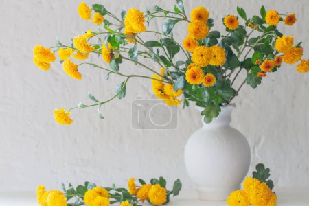 Foto de Crisantemos amarillos en jarrón blanco sobre fondo pared blanca vieja - Imagen libre de derechos
