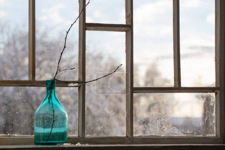 Téléchargez les photos : Bouteille en verre vert avec branche sur la vieille fenêtre d'hiver - en image libre de droit