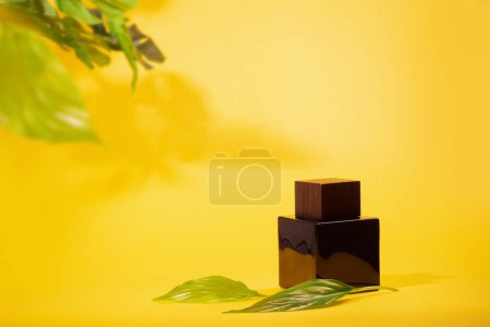 Foto de Frasco de perfume marrón con hojas verdes sobre fondo amarillo - Imagen libre de derechos