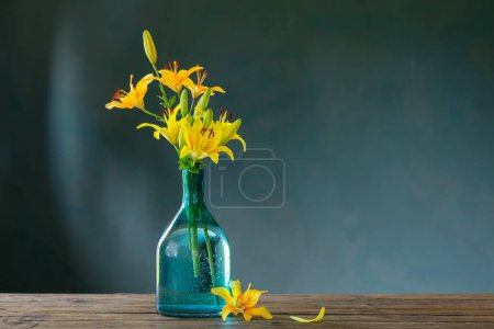 Photo for Yellow lilies in glass vase on dark background - Royalty Free Image