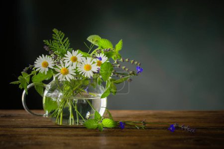 Foto de Ramo de flores de verano en tetera de vidrio sobre fondo oscuro, concepto de té de hierbas saludable - Imagen libre de derechos