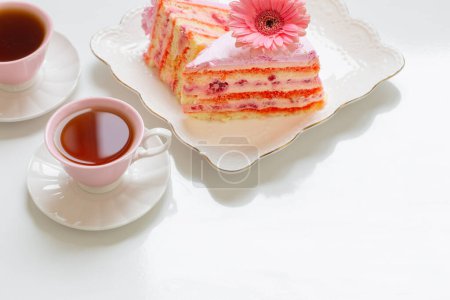 Téléchargez les photos : Deux tasses de thé avec gâteau rose sur table blanche - en image libre de droit