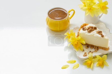 Foto de Tarta de queso con taza de té y flores amarillas de primavera sobre una mesa blanca - Imagen libre de derechos