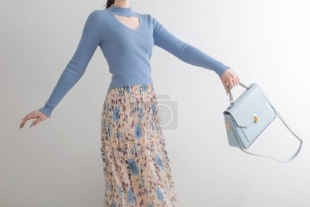 Téléchargez les photos : Jeune fille en chemisier bleu et jupe plissée avec sac à main bleu sur fond blanc - en image libre de droit