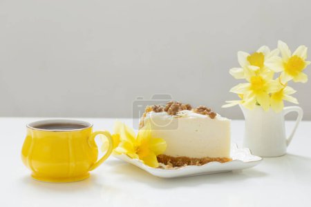 Téléchargez les photos : Gâteau au fromage avec tasse de thé et fleurs jaunes de printemps sur table blanche - en image libre de droit