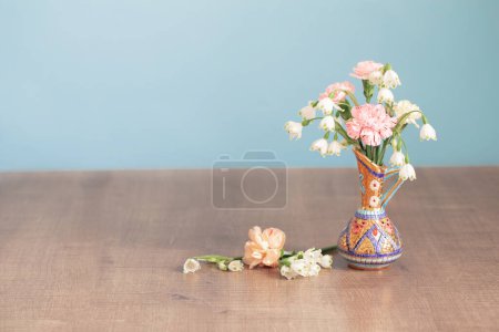 Foto de Flores en jarra vintage sobre mesa de madera sobre fondo azul - Imagen libre de derechos