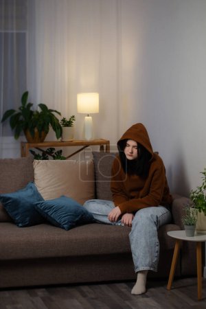 Foto de Triste adolescente chica sentado en sofá interior en la noche - Imagen libre de derechos