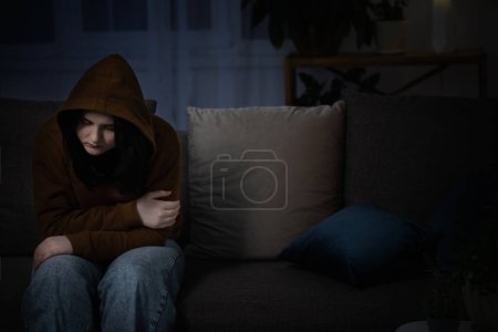Photo for Sad teenager girl sitting on couch indoor at night - Royalty Free Image