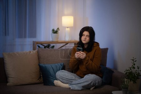 Foto de Chica adolescente con teléfono inteligente en el sofá por la noche - Imagen libre de derechos