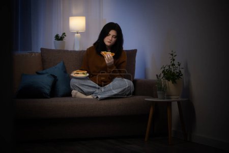 Photo for Teenage girl eating  sandwich at night on  couch - Royalty Free Image