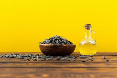 Photo for Oil and sunflower seeds on wooden table on  yellow background - Royalty Free Image