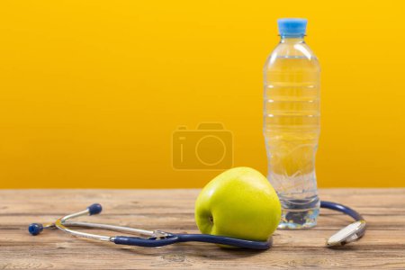 Téléchargez les photos : Bouteille d'eau avec pomme verte et stéthoscope sur table en bois - en image libre de droit