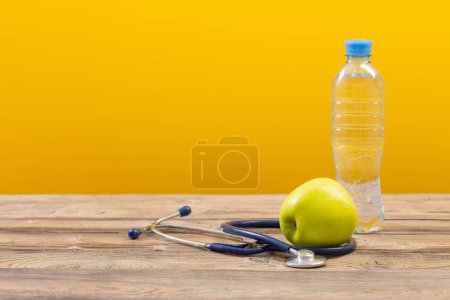 Photo for Bottle of water with green apple and stethoscope  on wooden table - Royalty Free Image