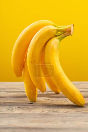 Foto de Ramo de plátanos sobre mesa de madera sobre fondo amarillo - Imagen libre de derechos