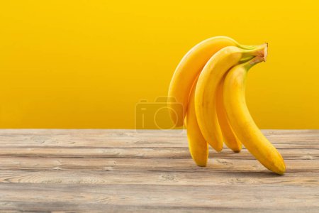 Téléchargez les photos : Bouquet de bananes sur table en bois sur fond jaune - en image libre de droit