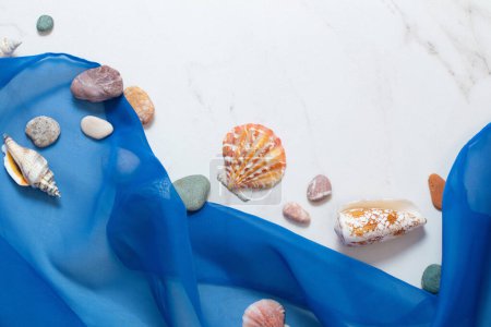 Photo for Sea background with blue cloth, stones, seashells on white marble - Royalty Free Image