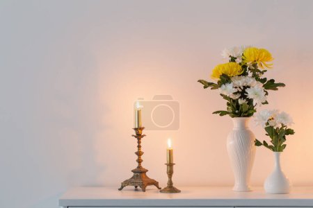 Téléchargez les photos : Chrysanthèmes fleurs dans des vases et des bougies brûlantes à l'intérieur blanc - en image libre de droit
