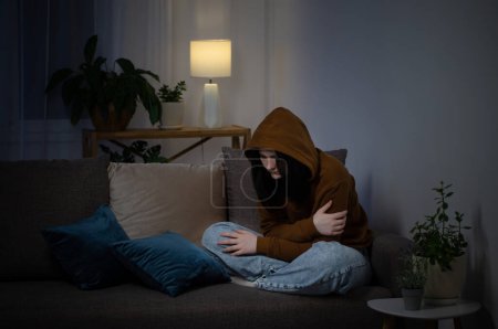 Téléchargez les photos : Triste adolescente assise sur le canapé intérieur la nuit - en image libre de droit