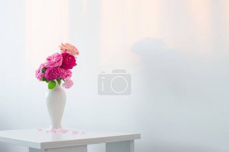 Foto de Rosas rosadas en jarrón blanco sobre la mesa sobre fondo pared blanca - Imagen libre de derechos