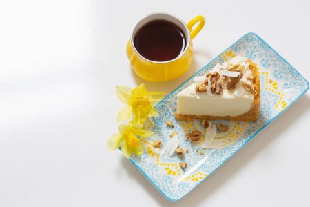 Téléchargez les photos : Tasse jaune de café avec gâteau au fromage et fleurs de printemps sur table blanche - en image libre de droit