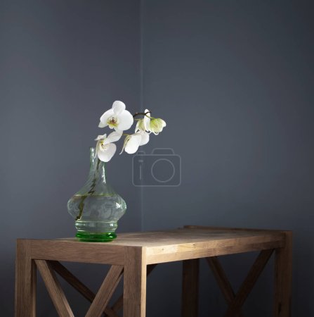 Foto de Orquídea blanca en jarrón de cristal vintage en estante de madera en la pared de fondo - Imagen libre de derechos