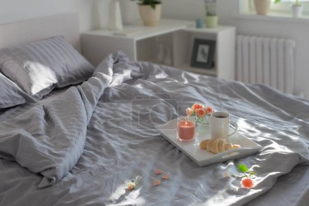 Téléchargez les photos : Tasse de café avec croissant et roses roses sur le lit dans la chambre - en image libre de droit